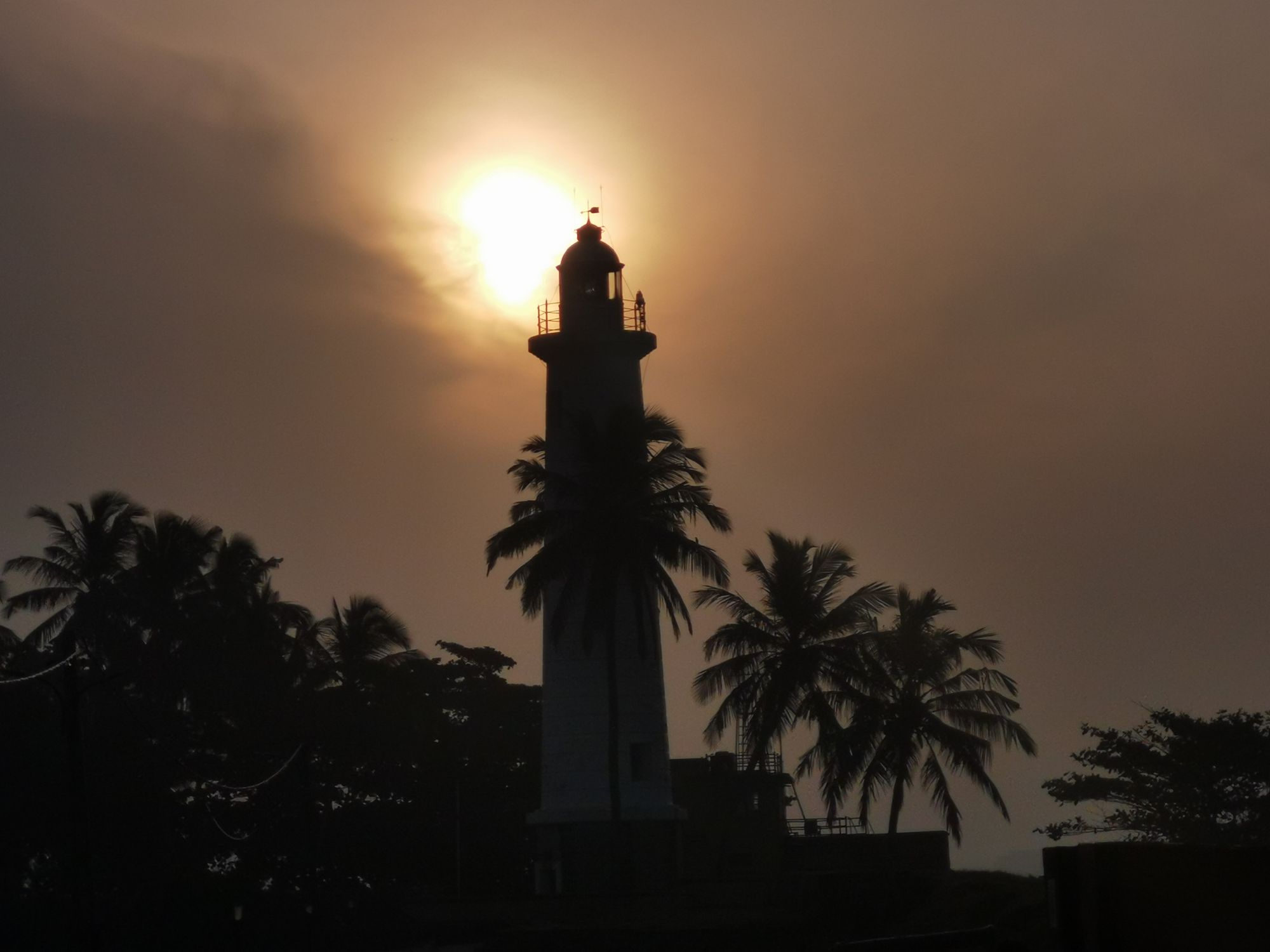 Galle Fort Lighthouse, Sri Lanka, during the evening surrounded by coconut trees and the evening sun in the background.