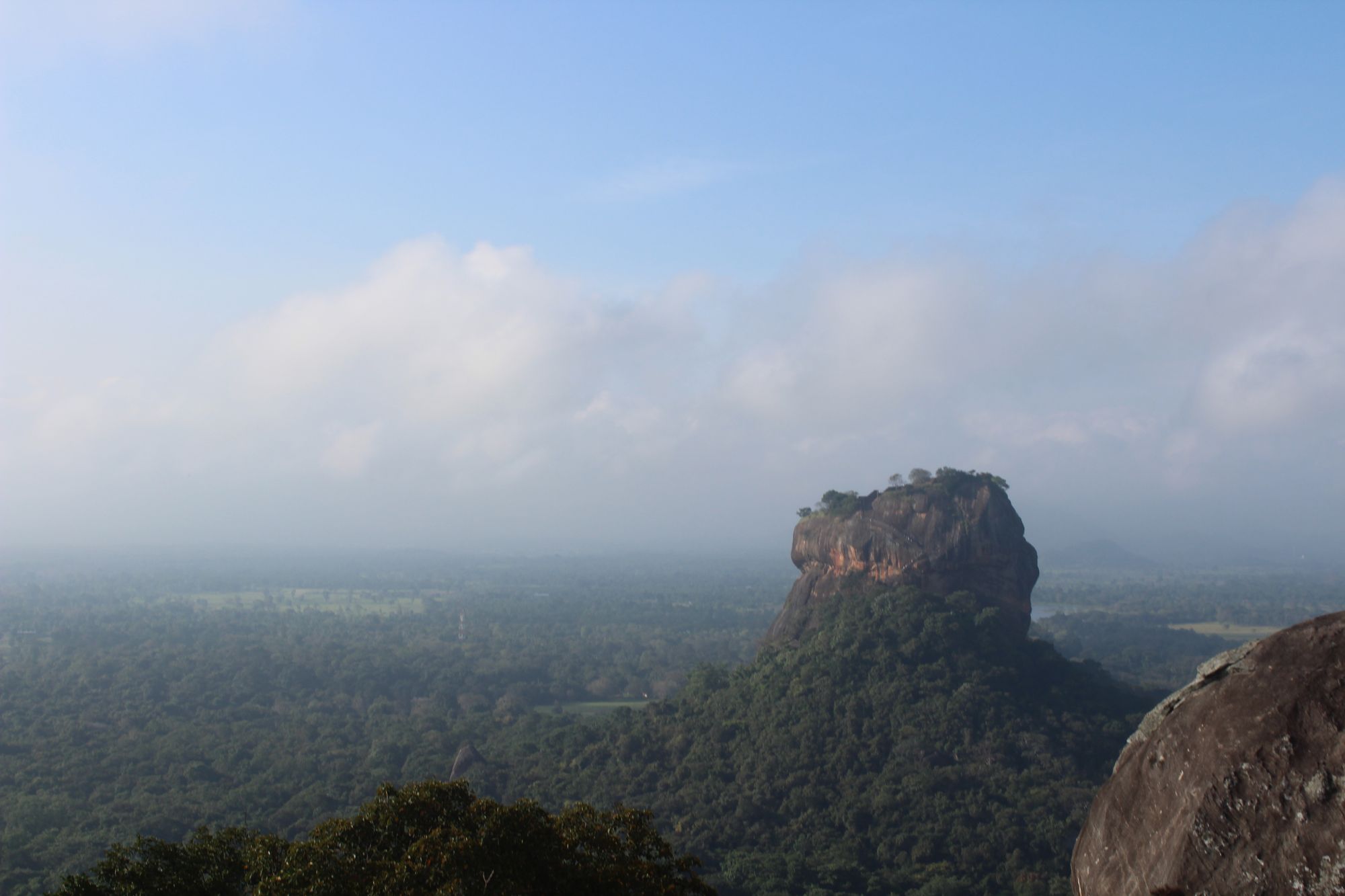 Sigiriya, the rock fortress in Sri Lanka, with the green plains of Dambulla in the background and a cloudy sky.