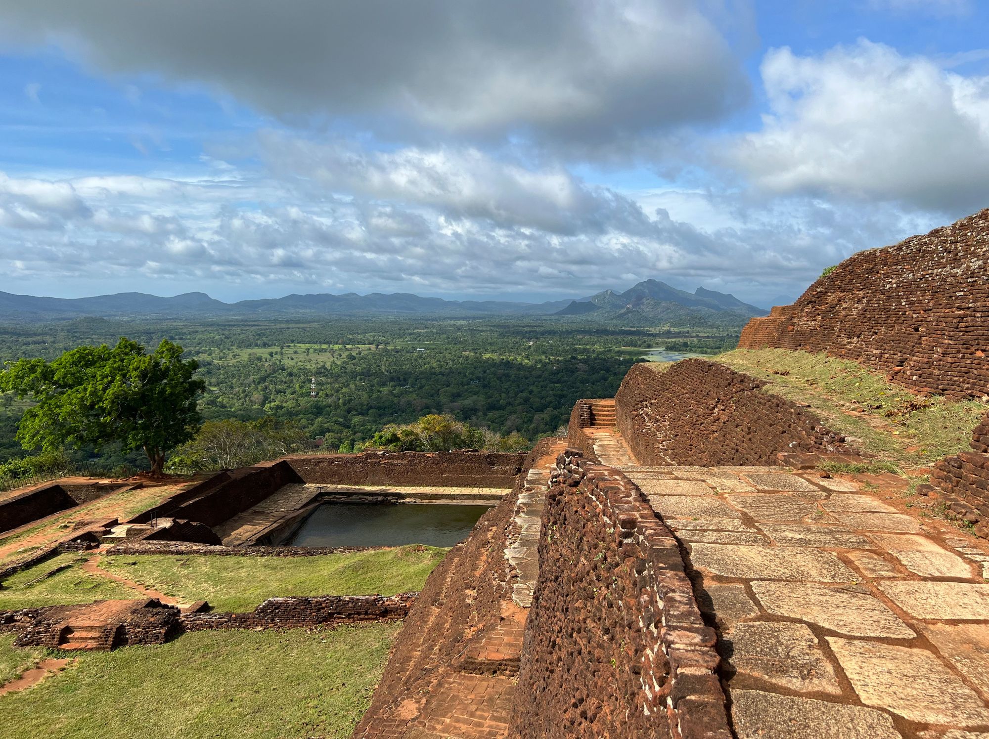 Ruins of the ancient palace in Sigiriya Rock, Sri Lanka, with palace walls and a water pond in sight.