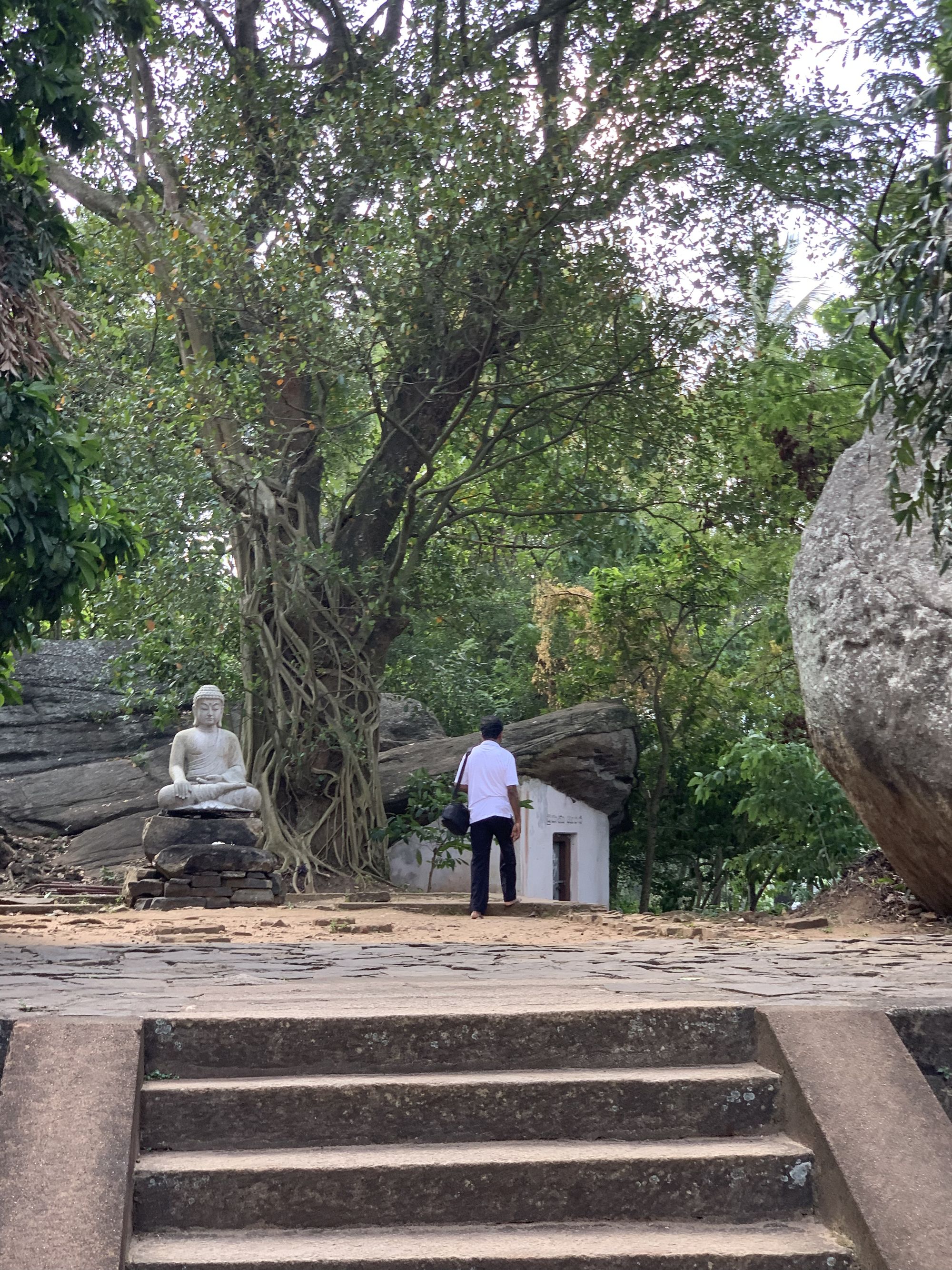 A man walking in a spiritual setting near Buddha statue, in Aluviharaya, Sri Lanka