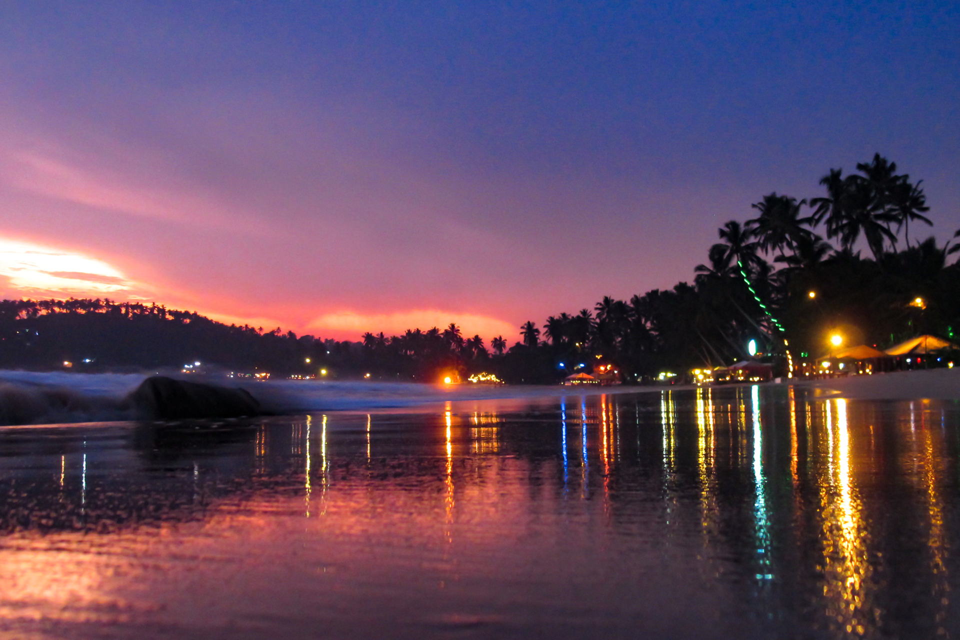 Mirissa Beach at night, seen with colorful lights, palm trees and calm sea.